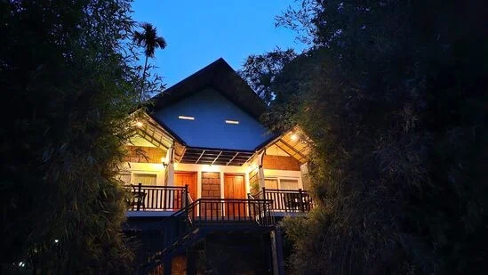 "Night view of the Twin Bedroom Pillar Cottage at Vintage Garden Resort, with soft outdoor lighting highlighting the traditional  pillars and surrounded by lush greenery under the starry sky."