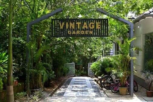 Elegant entrance to Vintage Garden Resort featuring a beautifully landscaped pathway, a welcoming arch adorned with vibrant flowers, and lush greenery, creating a warm and inviting ambiance